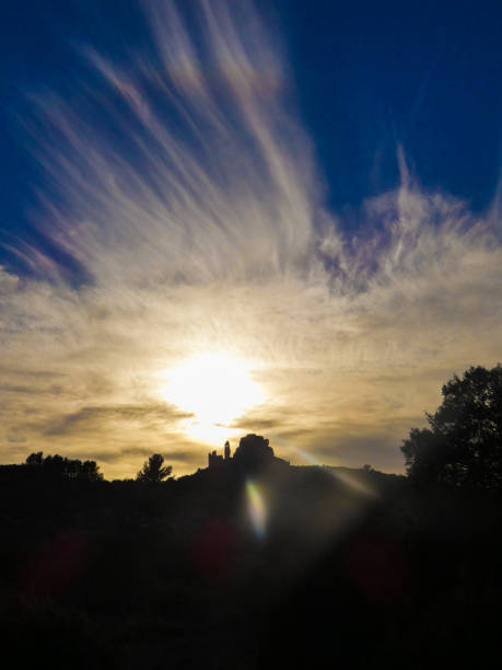 Photo of a magnificent landscape with a sunset that colors the clouds yellow with its light above the castle of Queen Jeanne. This photo was taken near Eyguieres in the Alpilles in Provence in France.