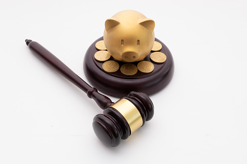 Golden Piggy bank and Judge's gavel, decorated with some coins, in front of a white background