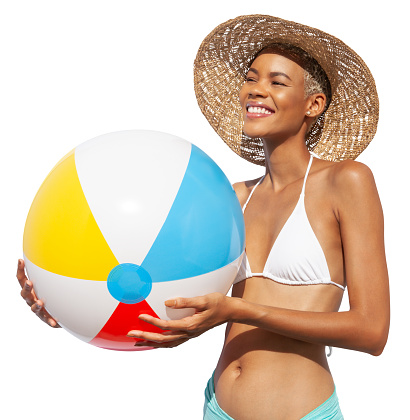 Smiling girl holds inflatable beach ball, wearing a sun hat and bikini, African latin American woman isolated on white background. Concept of a seaside holiday or shopping for a summer beach holiday