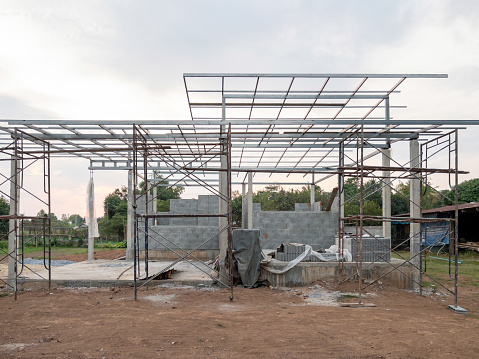 The unfinished house with the many scaffolding for construction in the countryside, front view with the copy space.