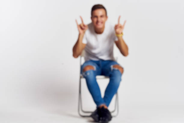 Man on a chair indoors torn jeans white t-shirt handsome face model light background. High quality photo