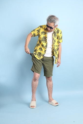 HAPPY SONGKRAN DAY. Asian tourist senior man in summer clothing with gesture of  broke or no money, empty pocket isolated on blue background.  Thai New Year's Day.
