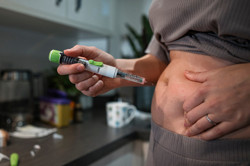 A close-up of a married LGBTQ woman injecting her stomach as part of her fertility treatment. She has cleaned and prepped the injection site ready for the injection. She is in the kitchen of her family home in the North East of England.
