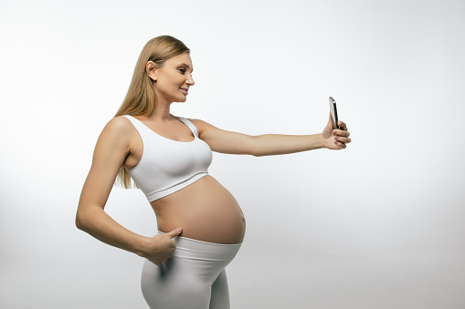 Pregnant woman with a phone. Pregnant woman in white top with a smartphone in hands
