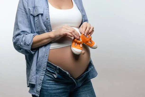 Baby-shoes. Pregnant woman with big belly holding baby-shoes in her hands