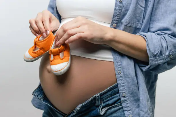Baby-shoes. Pregnant woman with big belly holding baby-shoes in her hands