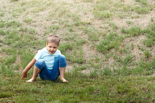 A cute six-year-old boy comes down from the mound and sits on a of dry grass.
