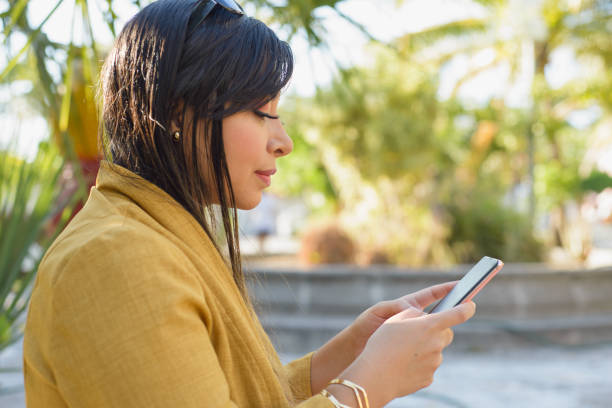 istock Woman sitting on a bench in a garden using her cellphone. 2099663765