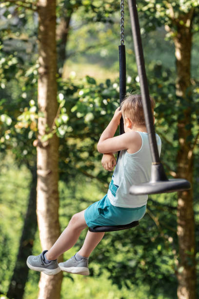 istock A small boy from behind on a journey through the forest between tall trees, with the help of a rope swing 2099663791