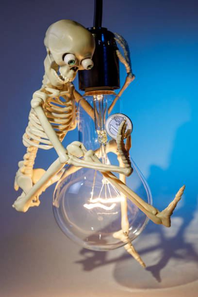 istock A funny and smart skeleton swinging on a light bulb, against a blue background, symbolize to save electricity. Free space for text 2099669606