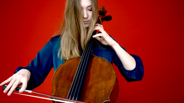 Artist plays with a bow on the strings of the cello in the red studio background
