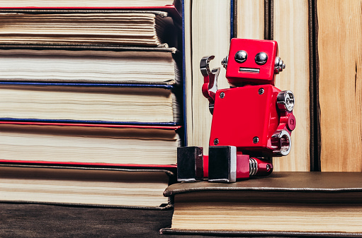 Photo of old antique books stack and row with sitting red robot toy, close up view.