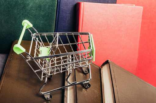 Photo of various colored books row with shopping cart. Book store concept.