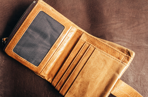 Photo of yellow opened leather wallet laying on brown leather material surface.