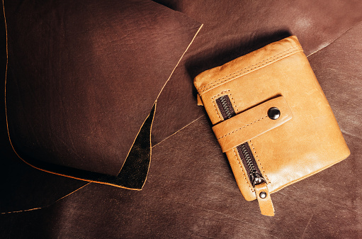 Photo of yellow leather wallet laying on brown leather roll material surface.