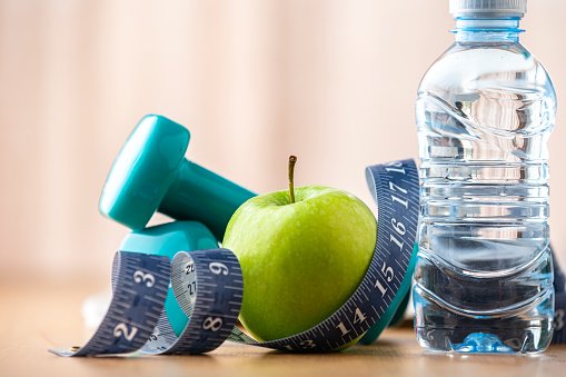 Exercising, healthy eating and fitness concept. Dumbbells, tape measure, water bottle, apple