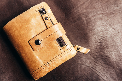 Photo of yellow leather wallet laying on brown leather material surface.