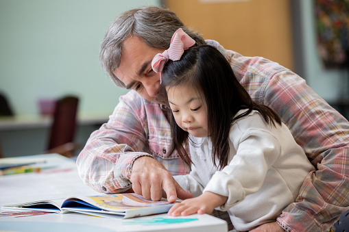 Little girl with Down Syndrome reads picture book with her adopted father