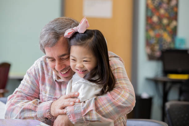 istock Father hugs his elementary age adopted daughter who has Down Syndrome while attending school function 2099688464