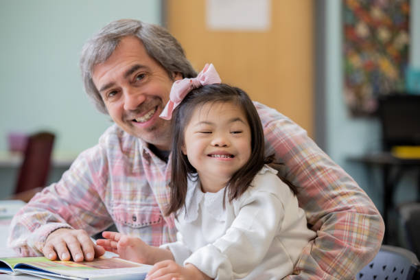 istock Father holds adopted daughter with Down Syndrome while they read a book in classroom 2099688466