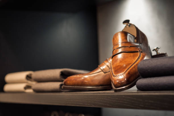 Shelf with brown handmade shoes and few folded sweater pullovers.
