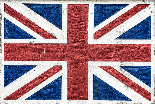 Close-up of a UK Union Flag painted on a stone surface, with visible weathering and signs of age and decline.