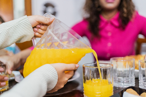 Close-up of a girl pouring orange juice into glass at home