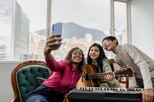 Mother taking selfie with children playing musical instruments at home