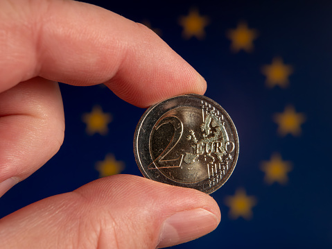 Close-up of a 2 Euro Coin Held Between Fingers with European Union Flag in the Background