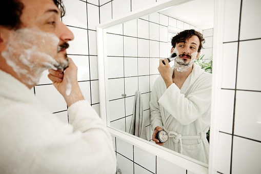 Young man shaving in the bathroom in the morning, daily routine.