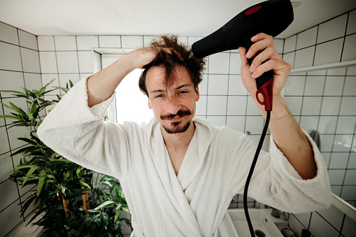 Reflection of a happy man drying his hair with hairdryer in bathroom.