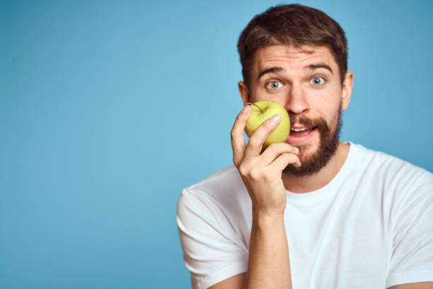 istock An energetic man with a green apple on a blue background gestures with his hands Copy Space emotions 2099771401