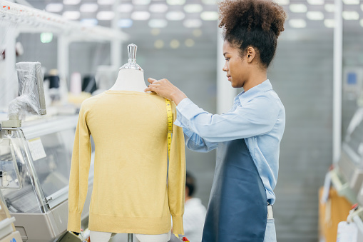 In the sewing industry using modern computerized machines. and half-body shot An American seamstress specialized in designing clothes for clients using mannequins and measuring tapes.