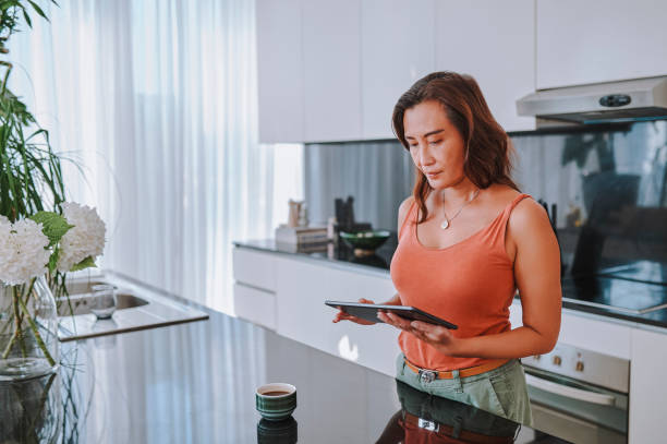istock Mature asian woman working on digital tablet in modern kitchen 2099808693