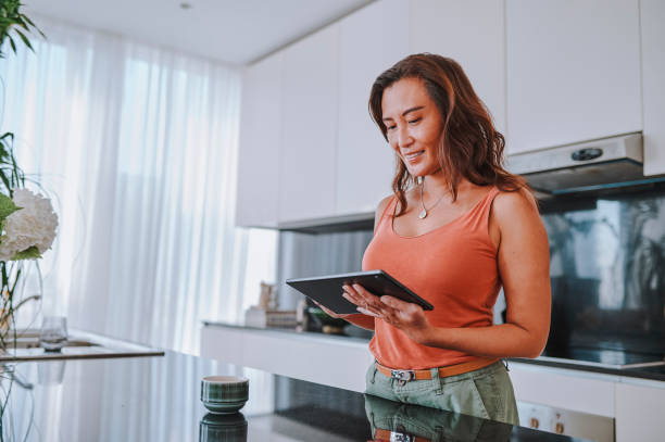 istock Low angle view of asian woman smiling, using digital tablet in modern kitchen 2099808699