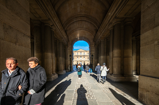 Visitors walking through the sunlit southern entrance of the Cour Carrée du Louvre in Paris.