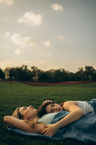 Beneath a canopy of endless sky, a daughter and her mother lay nestled in the embrace of the earth's verdant grass, their arms entwined in a tender clasp that spoke silently of unbreakable bonds and love's gentle caress.