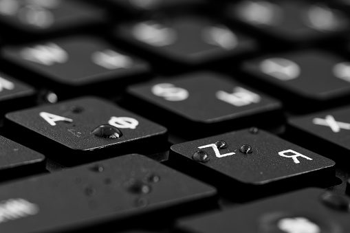 Close up view of  black keys with water drops. Black PC keyboard on a black background. English and cyrillic alphabet on the keyboard. Office, gaming concept. Advertising, presentation purposes