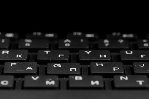 Close up view of  black keys. Black PC keyboard on a black background. English and cyrillic alphabet on the keyboard. Office, gaming concept. Advertising, presentation purposes