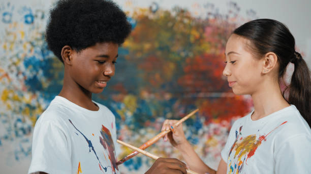istock Smiling diverse children paint color on each other shirt at wall. Edification. 2099855645