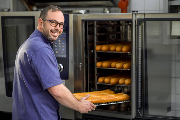 istock Baker in kitchen near oven with baguettes in bakehouse 2099860671