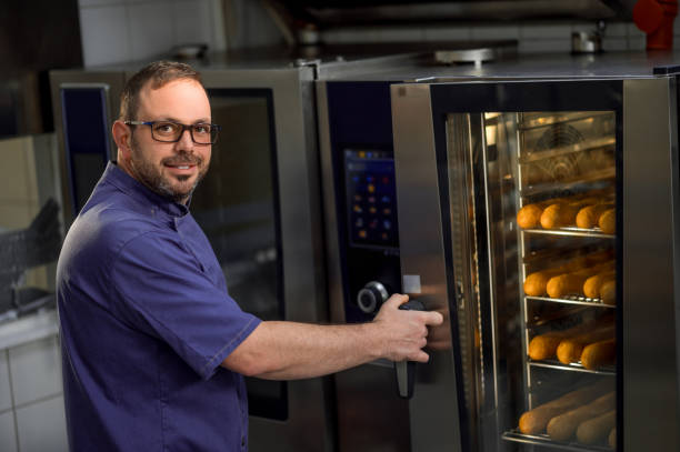 istock Baker in kitchen near oven with baguettes in bakehouse 2099860672