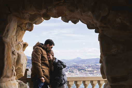 Father and daughter embracing each other under a stone archway with a panoramic cityscape in the background. Concept of natural and urban beauty.