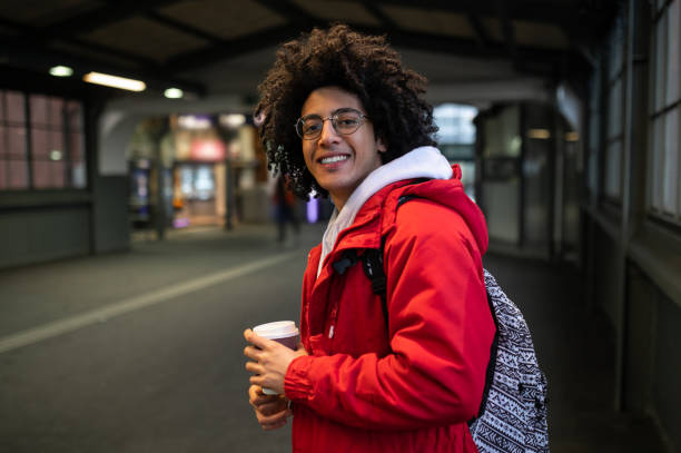 istock Curly-haired young guy at the railway platform with a coffee cup in hands 2099885697