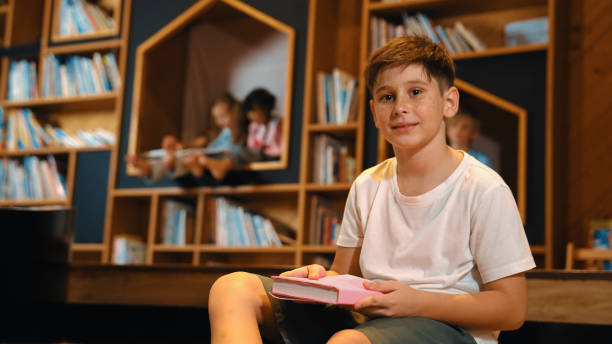 istock Boy look at camera while group of smart students sitting at library. Erudition. 2099891674