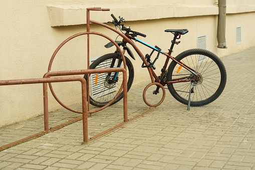 A bicycle secured with a bike lock is attached to a metal gate on the sidewalk.