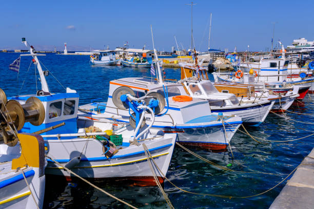 Colorful fishing boats line the harbor of the picturesque Greek island of Aegina, Greece at dusk, with the waterfront promenade in view at sunset.