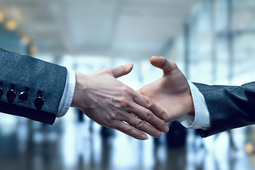 Businessmen reach out to shake hands against a blurred background of a business center.