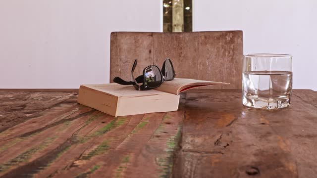 On a wooden table, a pair of glasses lies atop an open book, suggesting a pause in a reading session.
