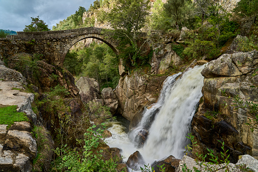 View of the ancient roman Ponte Mizarela, or Devils Bridge with a beautiful arch and picturesque waterfall, at the Peneda Geres National Park in Portugal, Europe